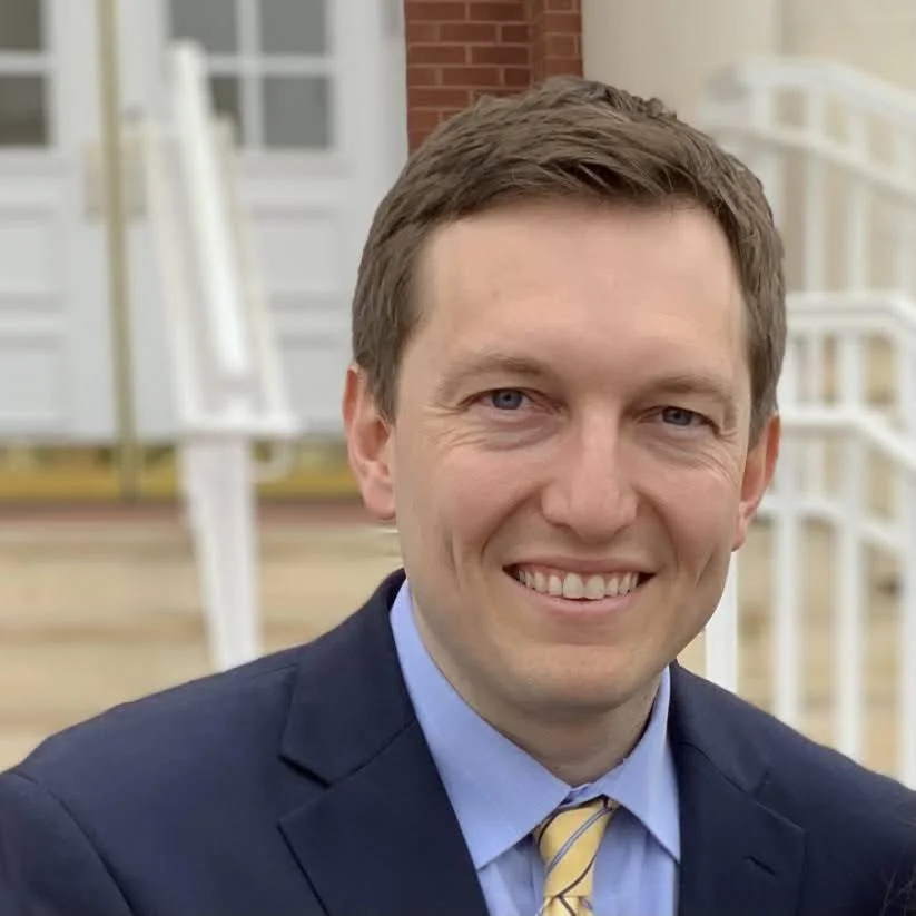 Smiling person in a suit and tie in front of a building.