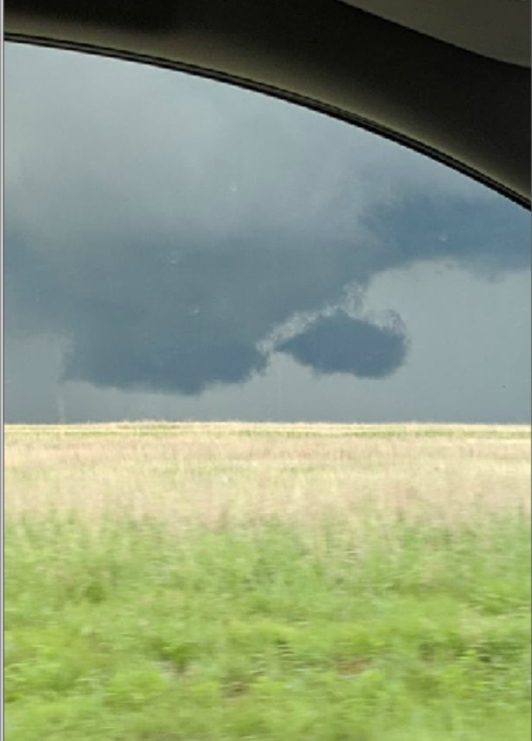 A dark, ominous cloud formation over an open field viewed from inside a car.