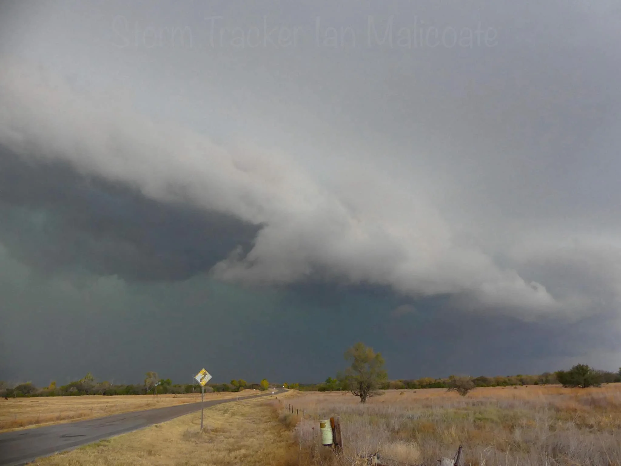 dark stormy sky above rural landscape with road and fields; large cloud formation indicating a storm