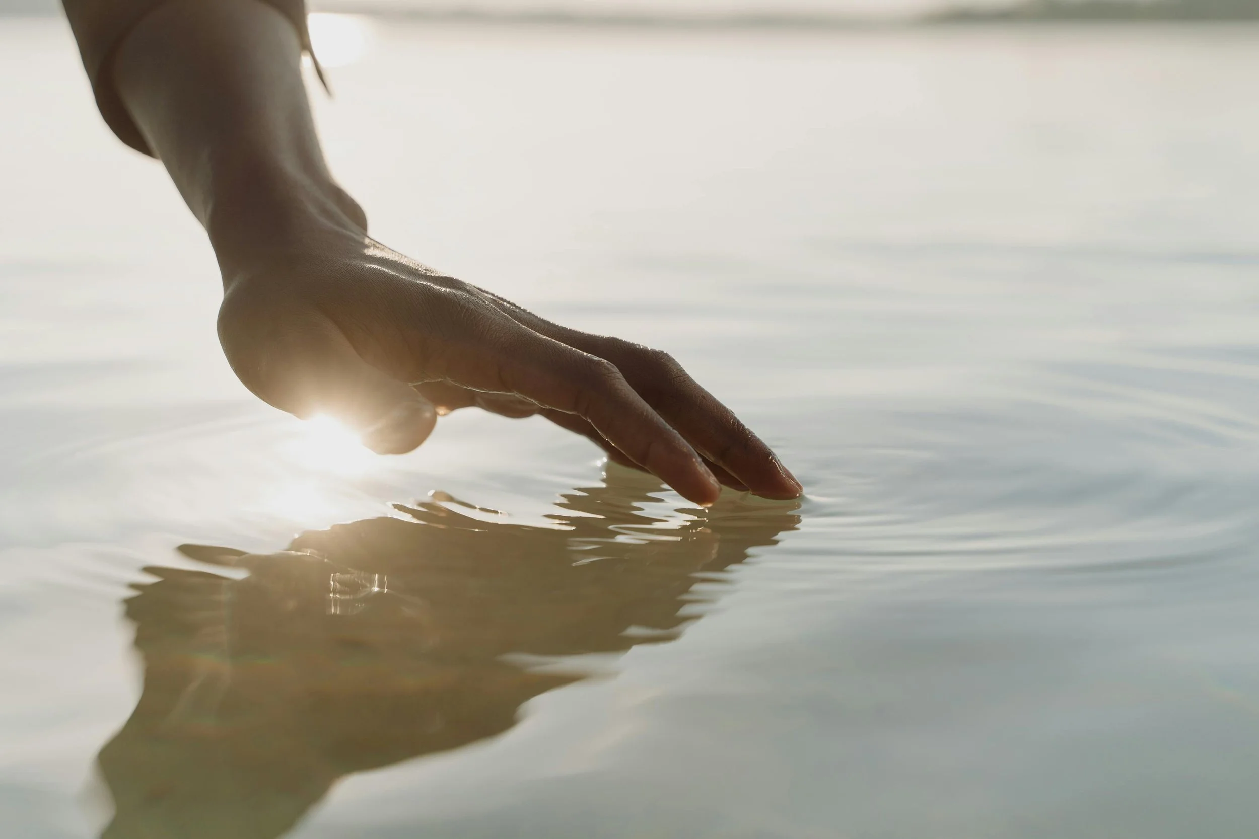 A close-up of a hand gently touching the surface of water during sunset. Trauma-informed therapist in Portland Oregon providing individual and couples therapy