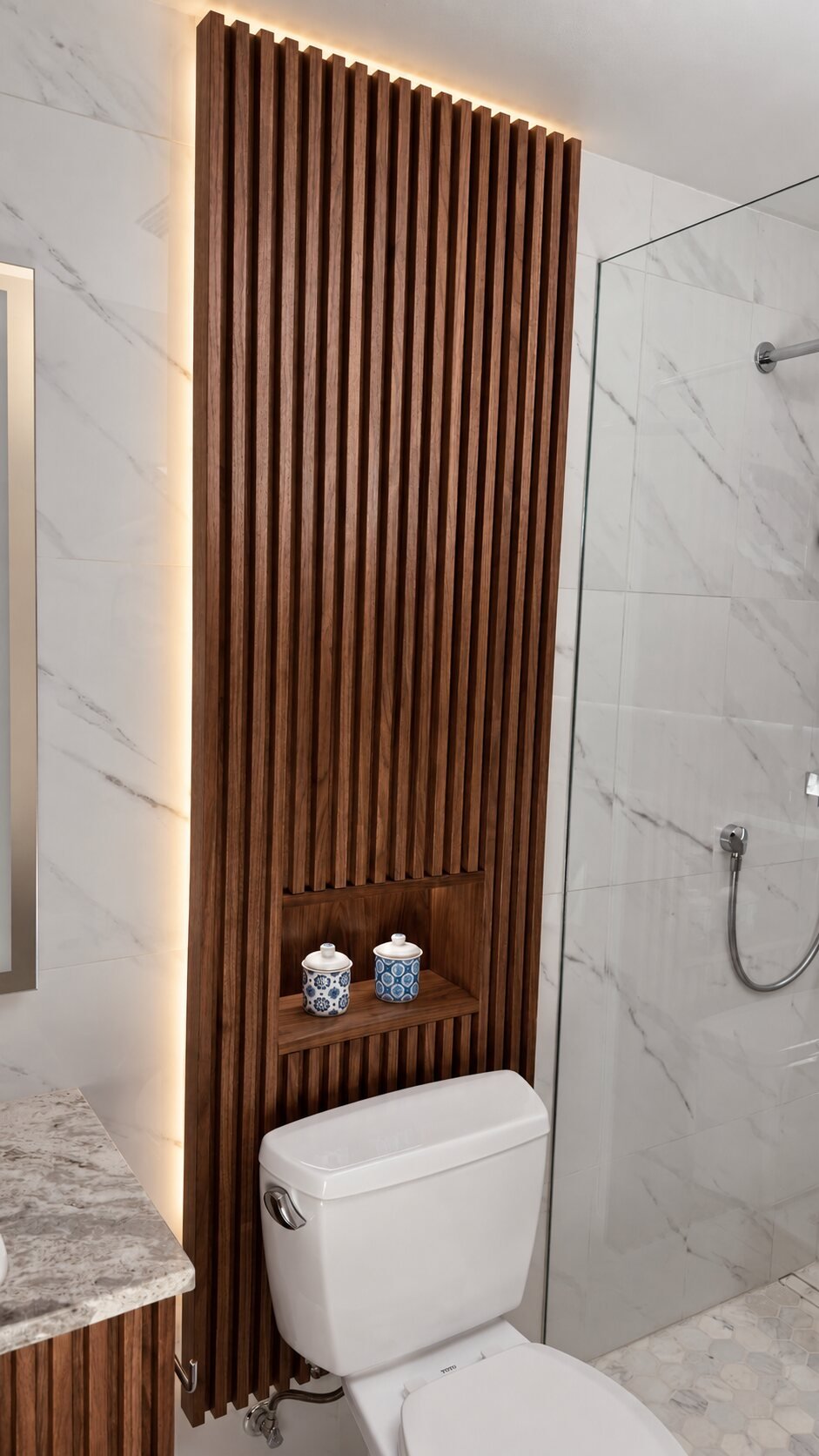 Floor to ceiling slatted walnut bathroom wall panel with concealed warm LED backlighting designed, built and installed by Motor City Woodshop Studio
