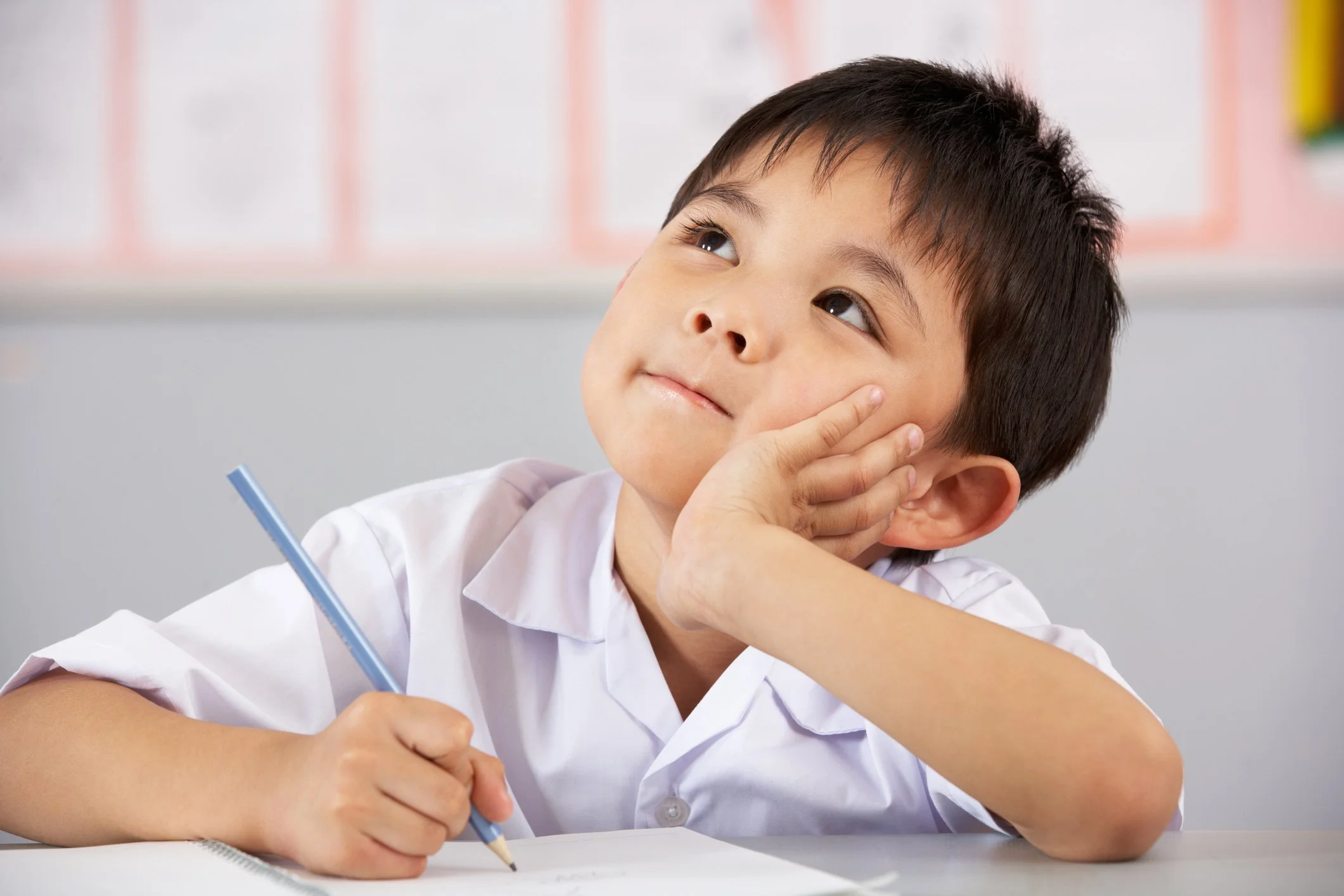 Elementary school-aged boy sitting at desk, appearing distracted during classwork