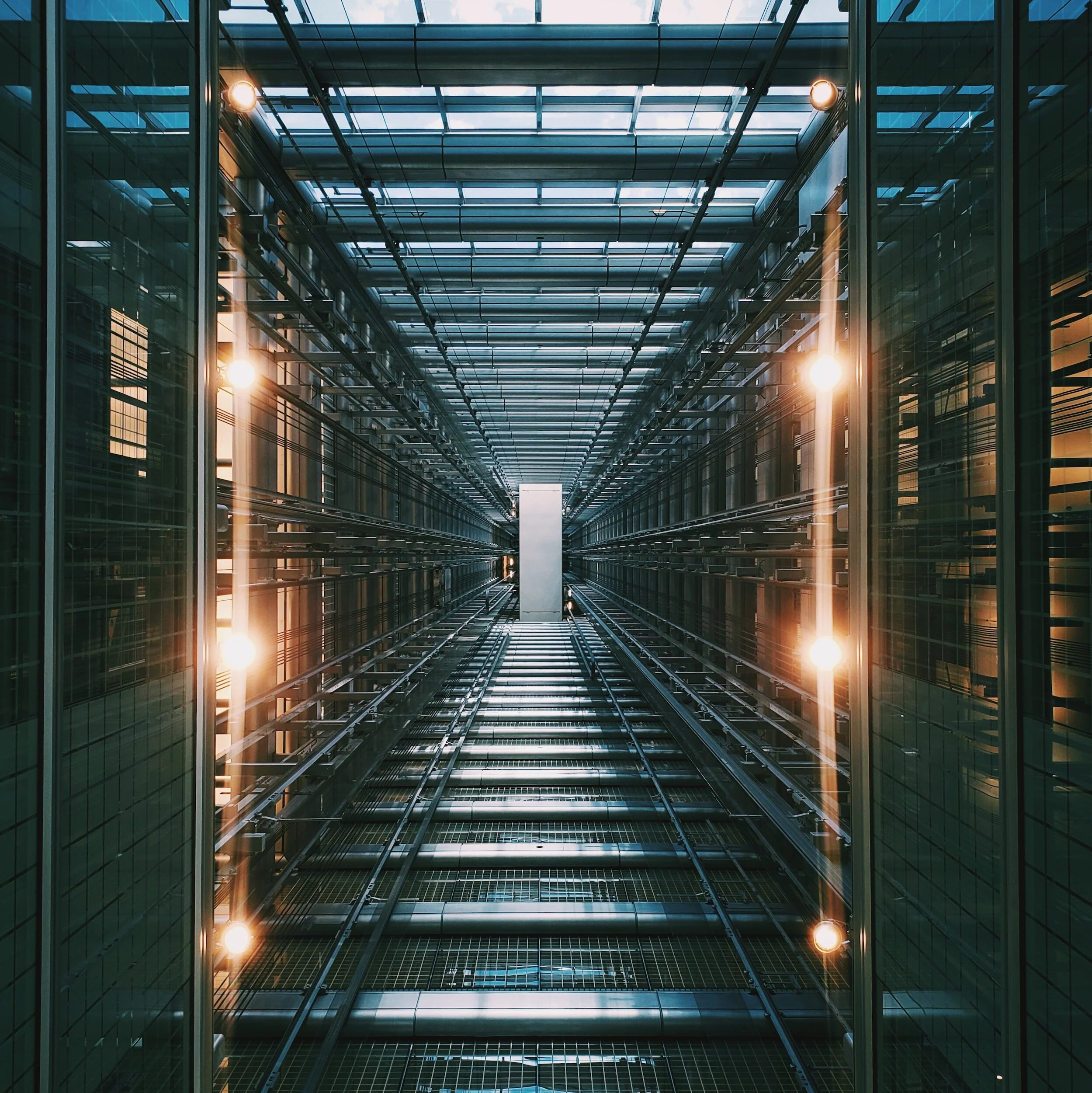 Interior of a modern glass elevator shaft with visible metal framework and lighting.