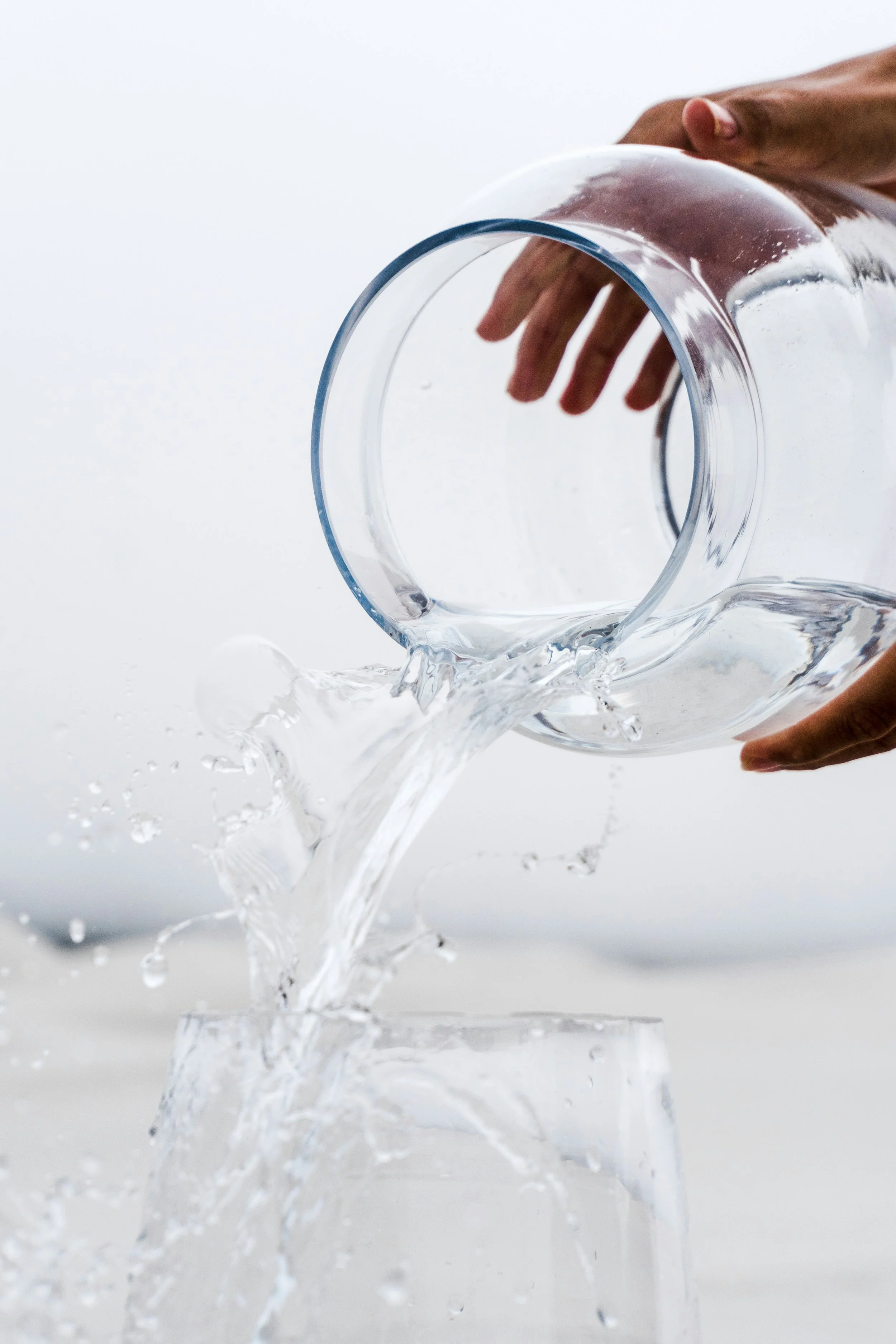 Image of a pair of male hands holding a clear jug of water and the water splashing out of the jug towards the forefront