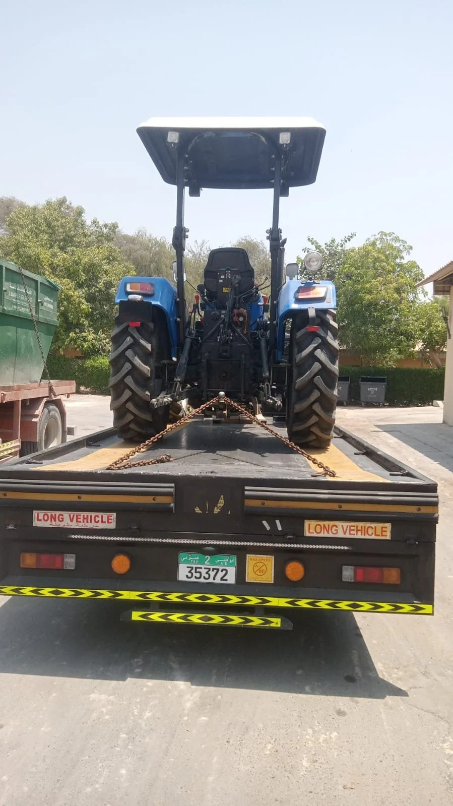 Flatbed recovery truck transporting a blue agricultural tractor secured with heavy-duty chains in Dubai