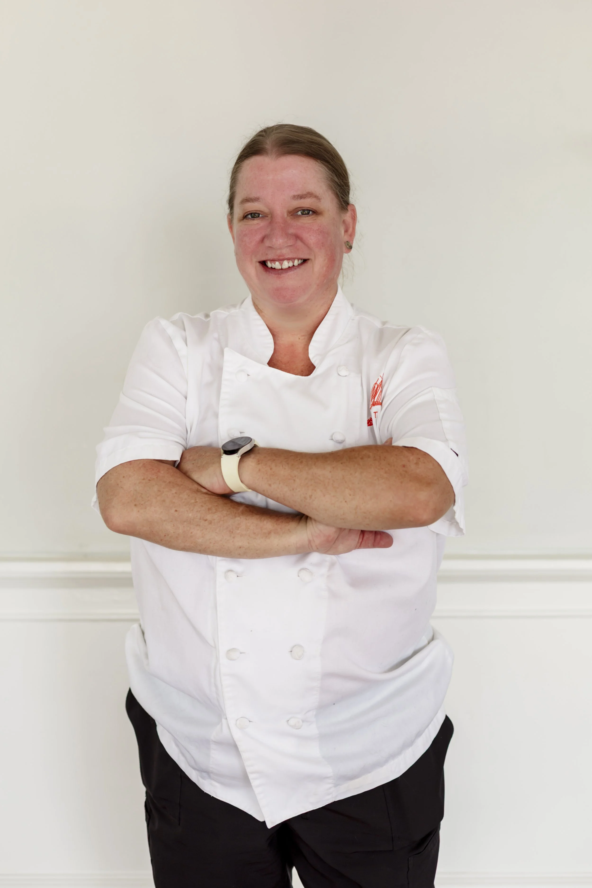A woman in a white chef's coat standing with her arms crossed against a plain white background.