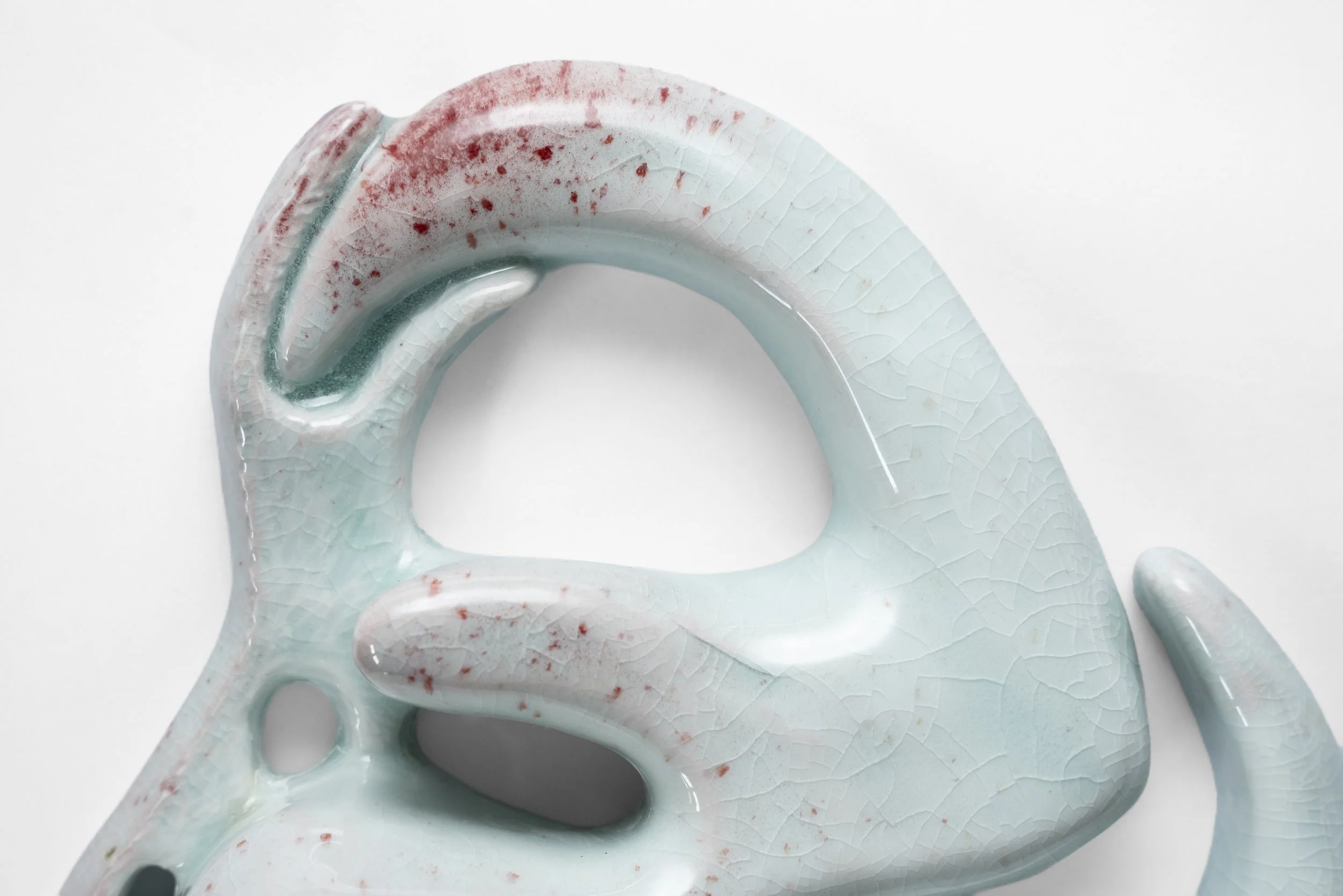 Top view of a glaze ceramic sculpture made out of porcelain with a light blue celadon glaze and spray of red at the top.