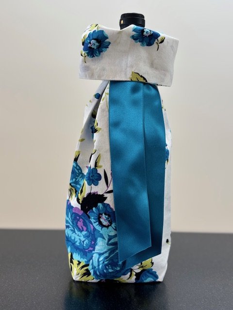 Upcycled fabric bottle bag in floral pattern in shades of bright blue on a white background. Lining matches outside of bag. Bag has bright blue satin ribbon.