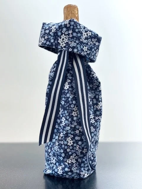 Upcycled fabric bottle bag in small floral pattern in shades of blue and white. Lining matches outside of bag. Bag has navy and white striped ribbon.