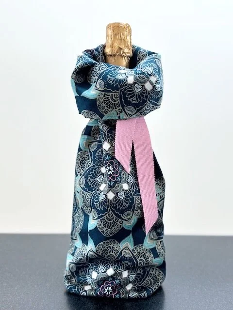Upcycled fabric bottle bag in a pattern of overall floral medallions in shades of blue with touches of rose. Lining matches outside of bag. Bag has rose ribbon.