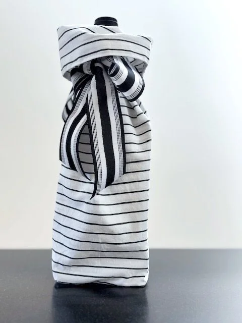 Upcycled fabric bottle bag in pattern of thin charcoal lines. Lining matches outside of bag. Bag has charcoal and white striped ribbon.