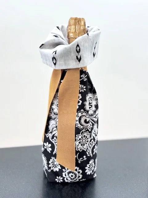 Upcycled fabric bottle bag in black and white floral pattern. Bag lined in black and white irate fabric. Bag has solid gold colored ribbon.