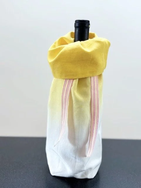 Upcycled fabric bottle bag in yellow ombre pattern - dark yellow at top fading to white at base. Lining matches outside of bag. Bag has pink, white and yellow striped ribbon.