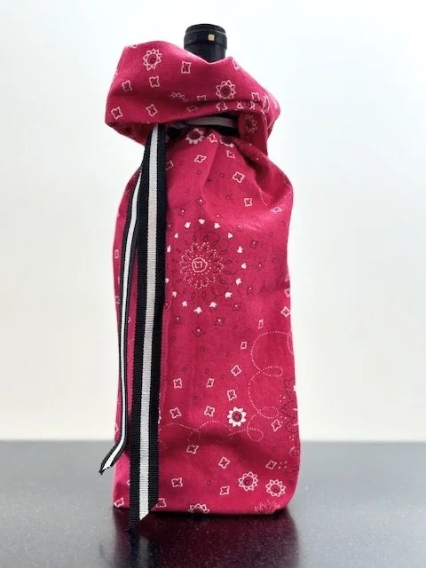 Upcycled fabric bottle bag in red bandana pattern. Lining matches outside of bag. Bag has black and white striped ribbon.