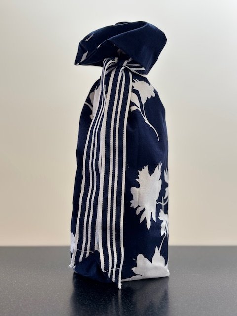 Upcycled fabric bottle bag in bold white floral pattern on navy background. Lining matches outside of bag. Bag has navy and white striped ribbon.