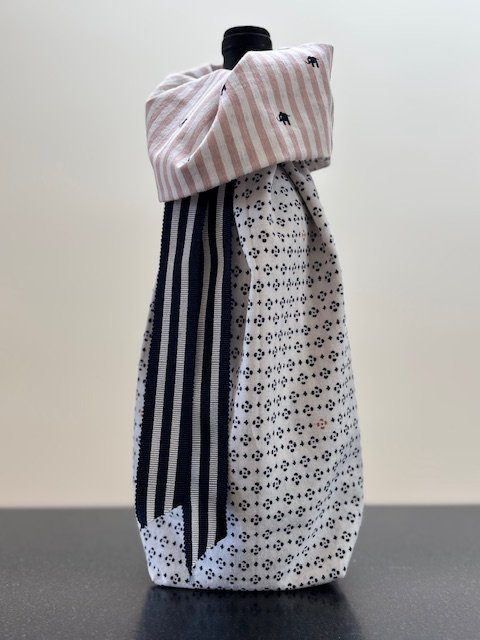Upcycled fabric bottle bag in small navy pattern on field of white. Bag lined in pink and white stripe with blue elephants. Bag has navy and white striped ribbon.