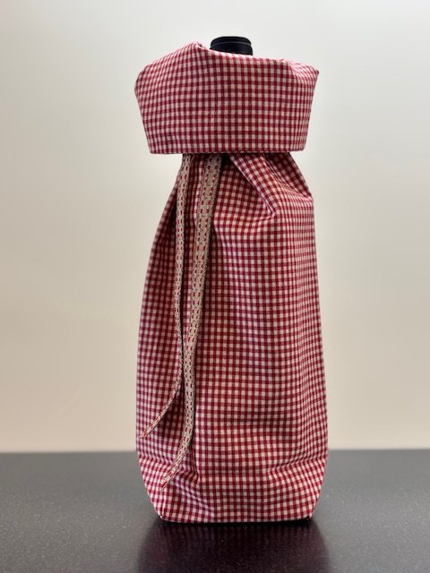 Upcycled fabric bottle bag in dark red and white gingham pattern. Lining matches outside of bag. Bag has tan and red patterned ribbon.
