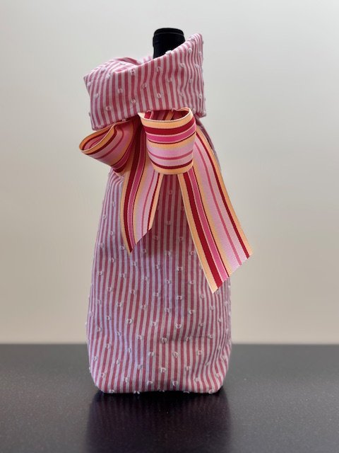 Upcycled fabric bottle bag in pink and white vertical stripe. Lining matches outside of bag. Bag has pink, orange, red striped ribbon.