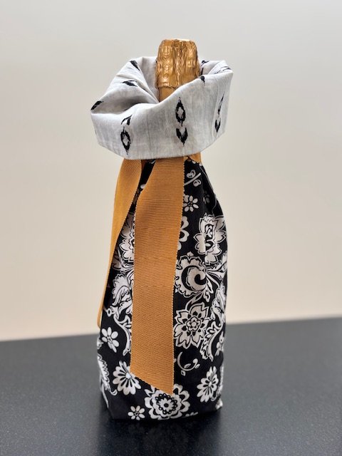 Upcycled fabric bottle bag in black and white floral pattern. Bag lined in black and white irate fabric. Bag has solid gold colored ribbon.