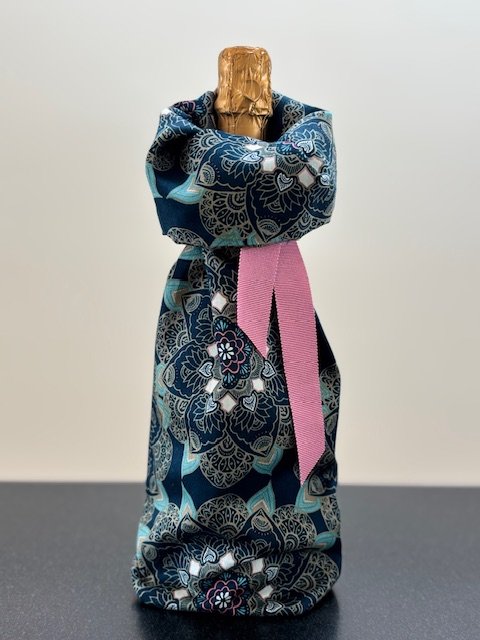 Upcycled fabric bottle bag in a pattern of overall floral medallions in shades of blue with touches of rose. Lining matches outside of bag. Bag has rose ribbon.