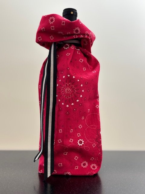 Upcycled fabric bottle bag in red bandana pattern. Lining matches outside of bag. Bag has black and white striped ribbon.