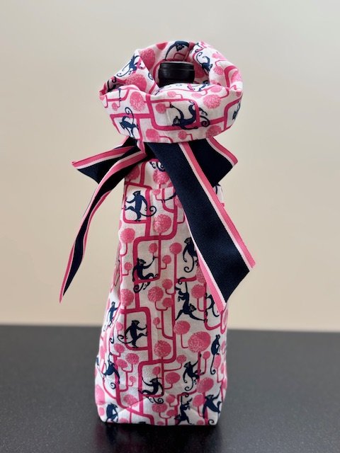 Upcycled fabric bottle bag in whimsical pattern of navy monkeys climbing on bright pink tress on a white background.Lining matches outside of bag. Bag has navy, pink and white striped ribbon.