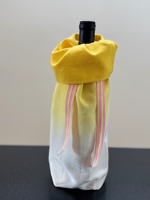 Upcycled fabric bottle bag in yellow ombre pattern - dark yellow at top fading to white at base. Lining matches outside of bag. Bag has pink, white and yellow striped ribbon.