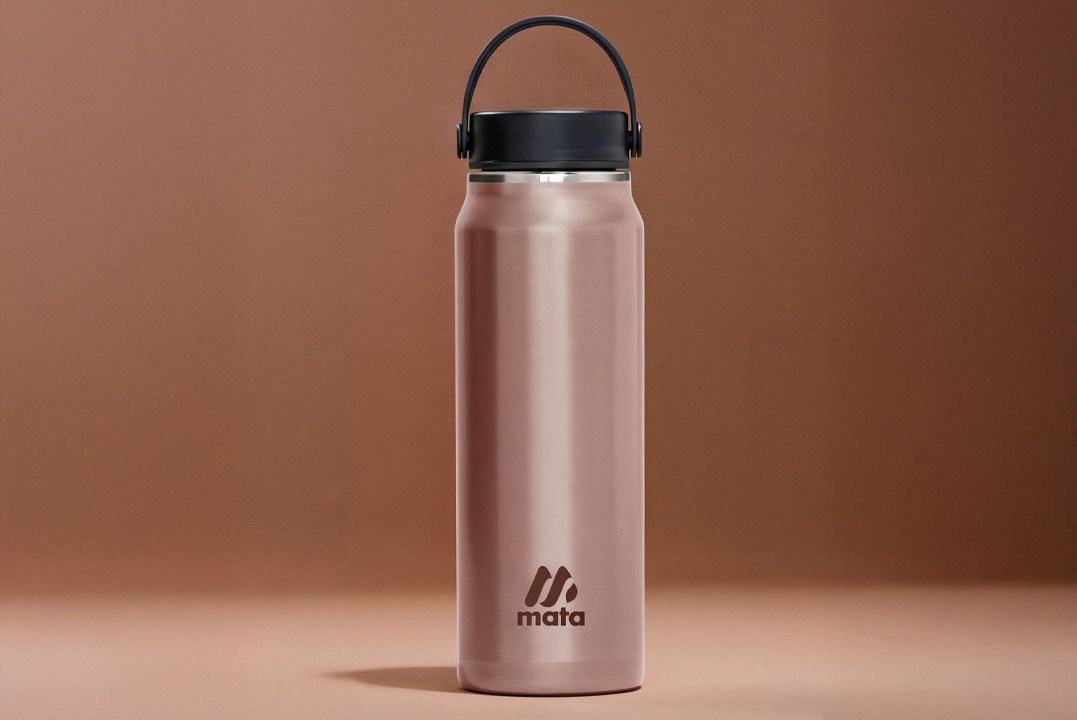 A pink matte water bottle with a black lid and handle, standing on a beige surface against a brown background.