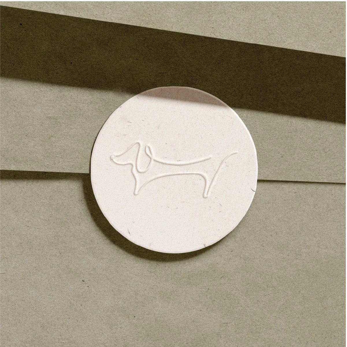 A round, pale-colored tablet with a cursive dog logo embossed on it, placed against a beige background with shadow.