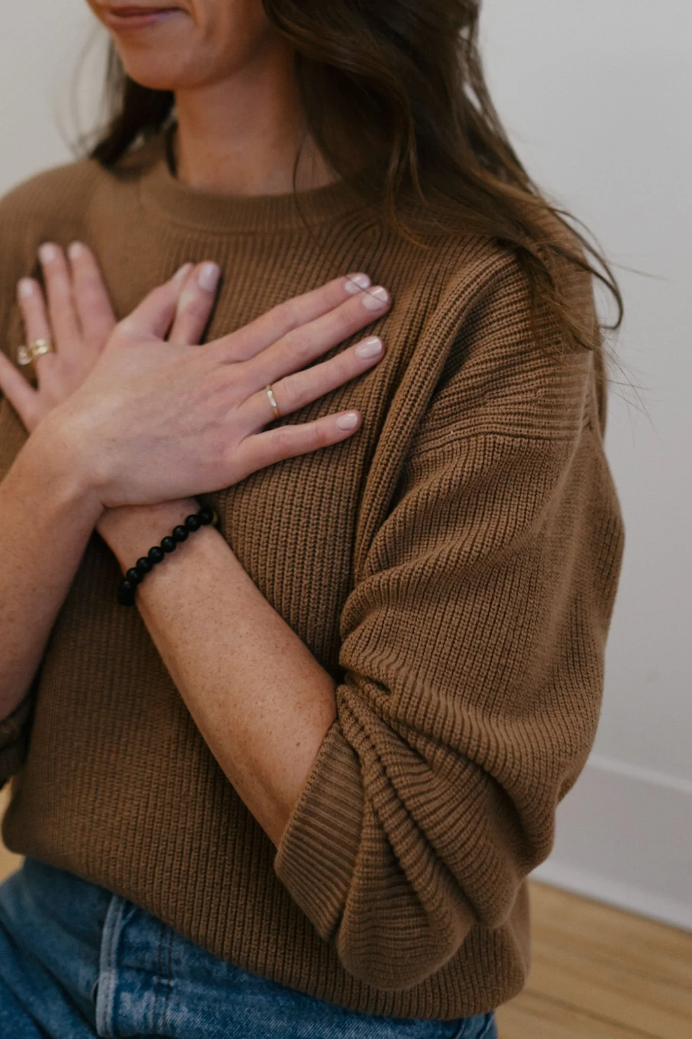 Michelle Ham wearing a brown sweater with hands crossed on chest; offering somatic strategies to support with therapy.