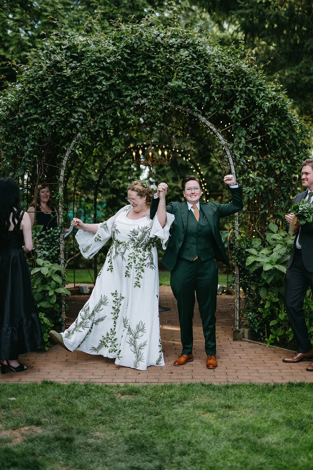 A queer couple cheers after their wedding ceremony at a beautiful garden venue near Eugene, Oregon