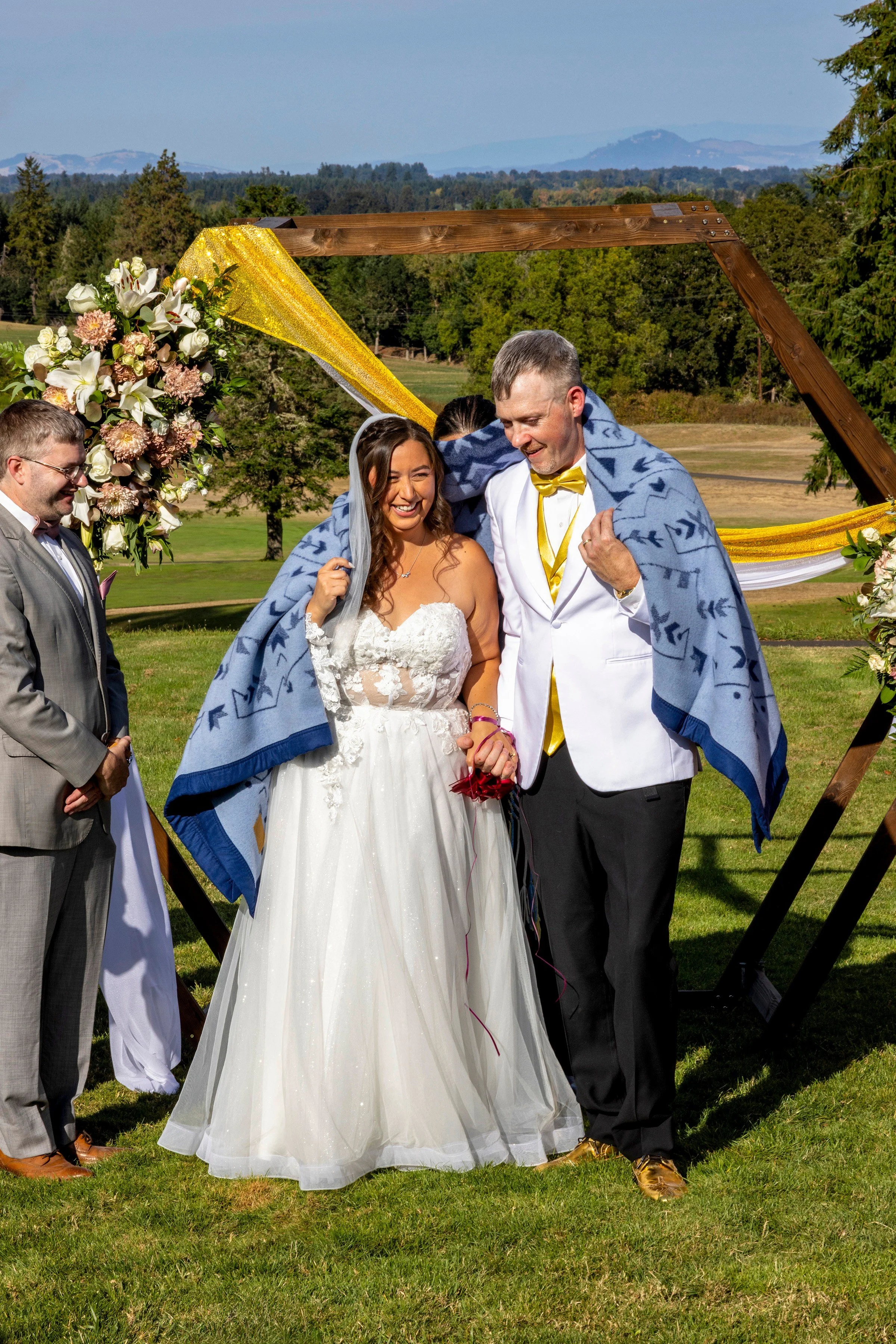 A newly married couple smile at their wedding guests when a traditional blanket is draped over their shoulders at the altar to honor the brides' native american heritage