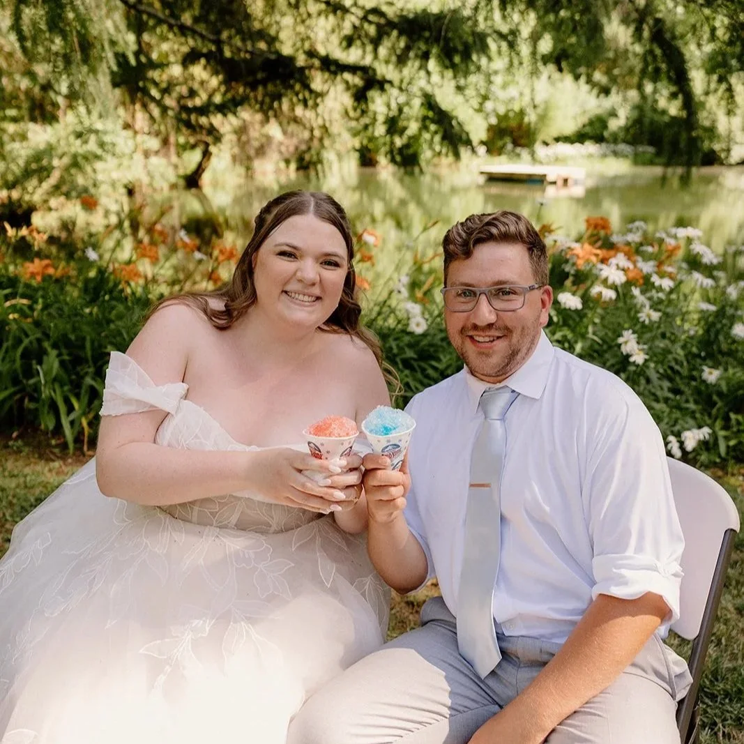 A wedding couple grins while holding their frozen snow cone treats on a hot July day.
