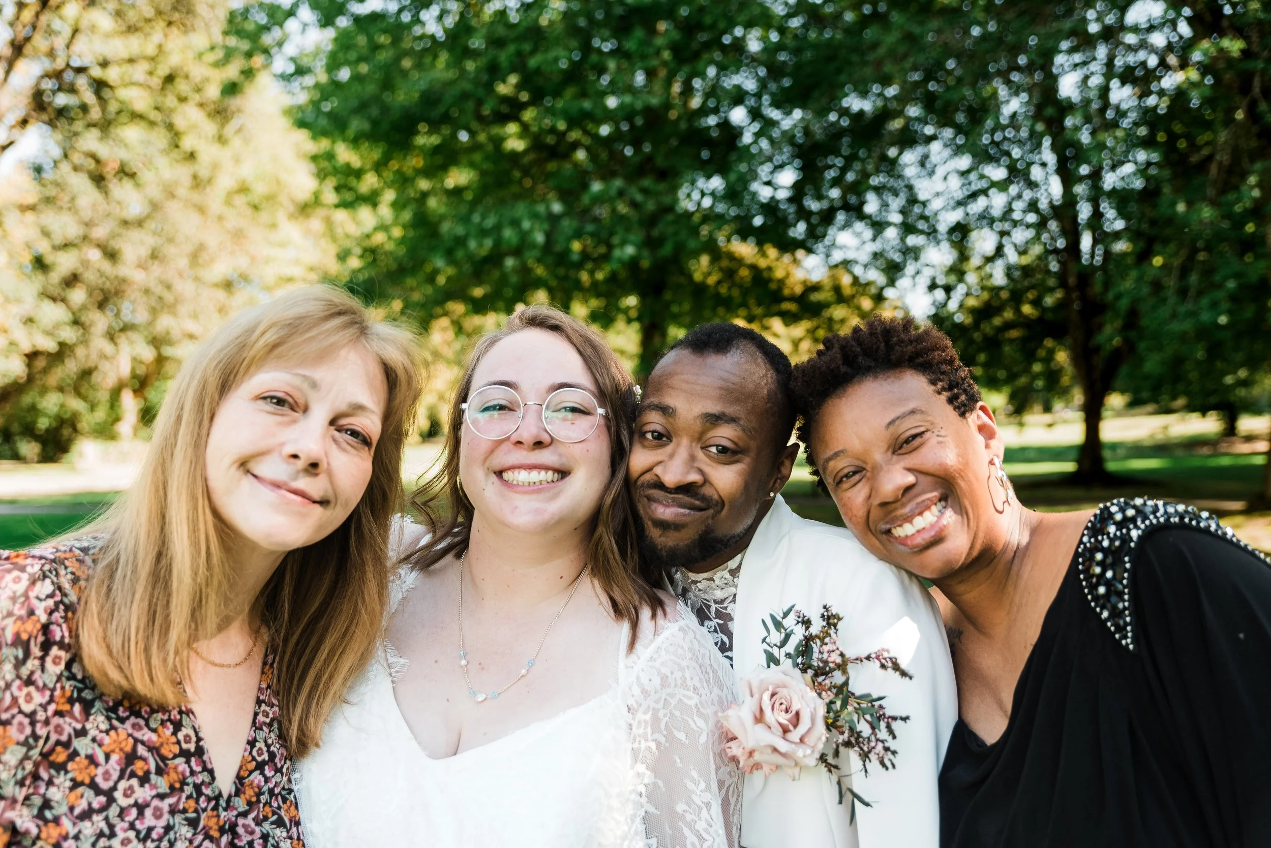 Newlyweds grin on their wedding day with their mothers at a public park in Eugene, Oregon