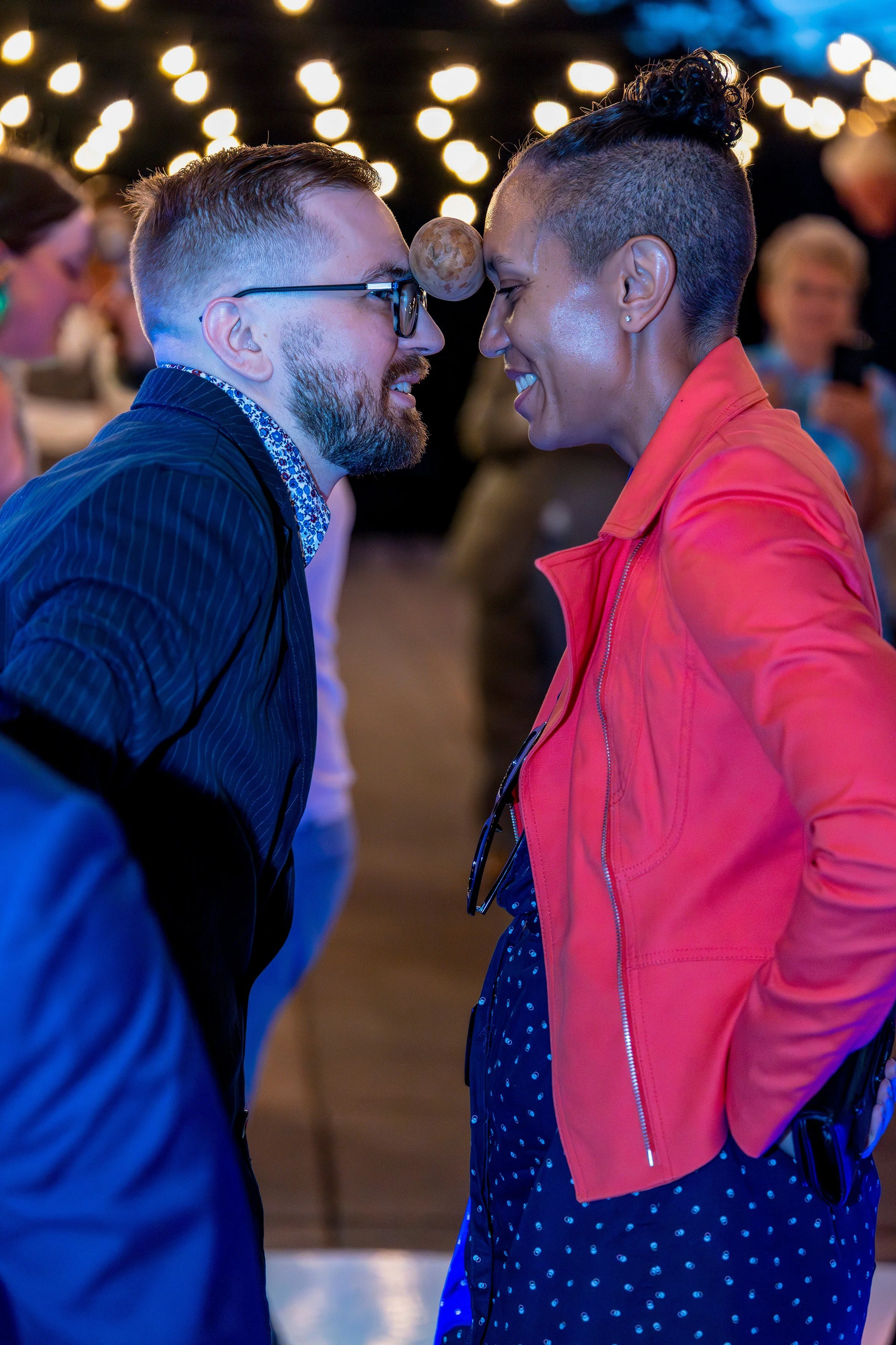 Two wedding guests grin at each other while balancing a potato between their foreheads during a traditional potato dance