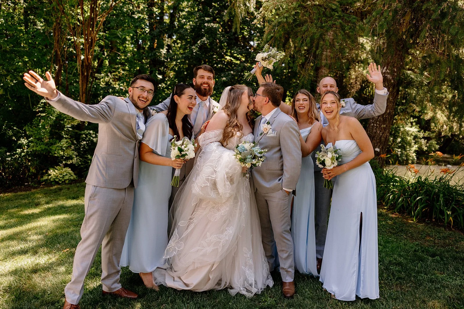 Newlyweds kiss surrounded by their cheering wedding party at Ron's Pond near Eugene, Oregon