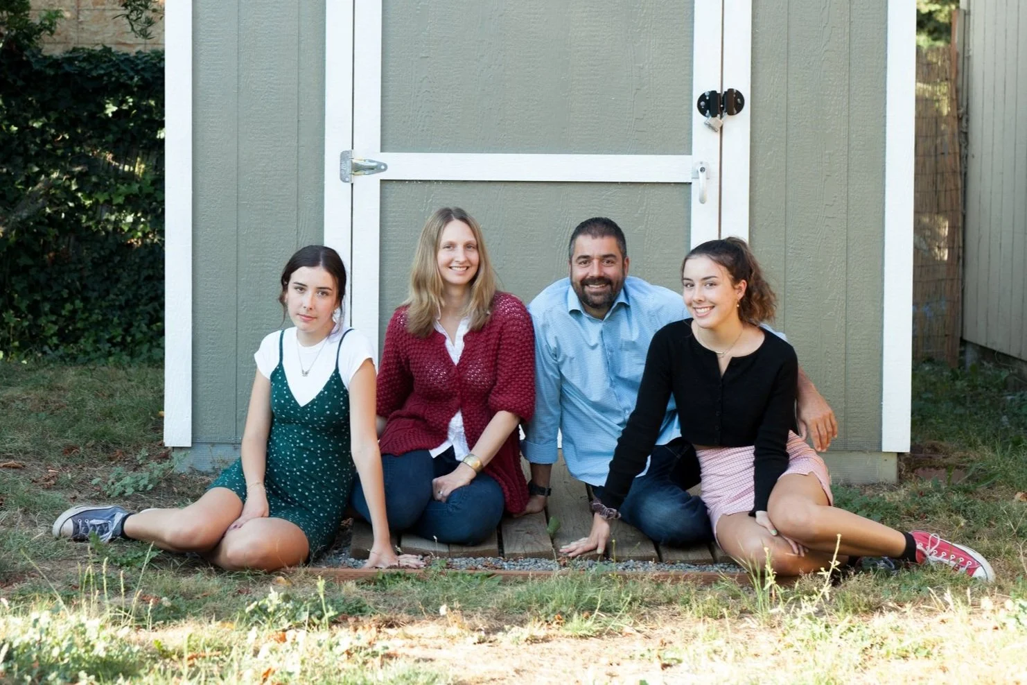 BIPOC Family of 4 sitting in front of a shed at their new home