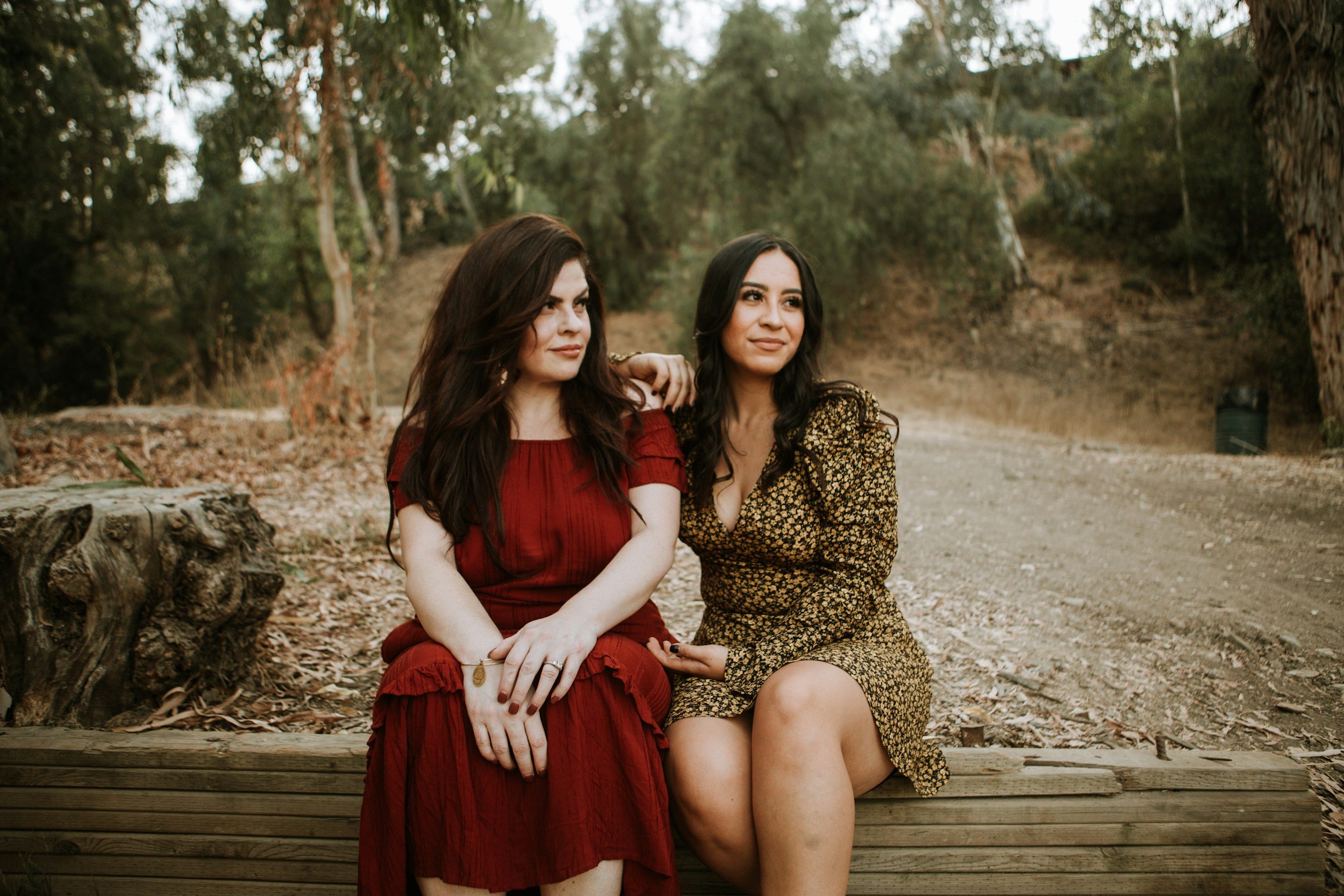 Two women sitting together on wooden bench in nature — LGBTQIA+ affirming therapy for queer and trans women, men, and nonbinary people in relationships, and identity exploration in Los Angeles