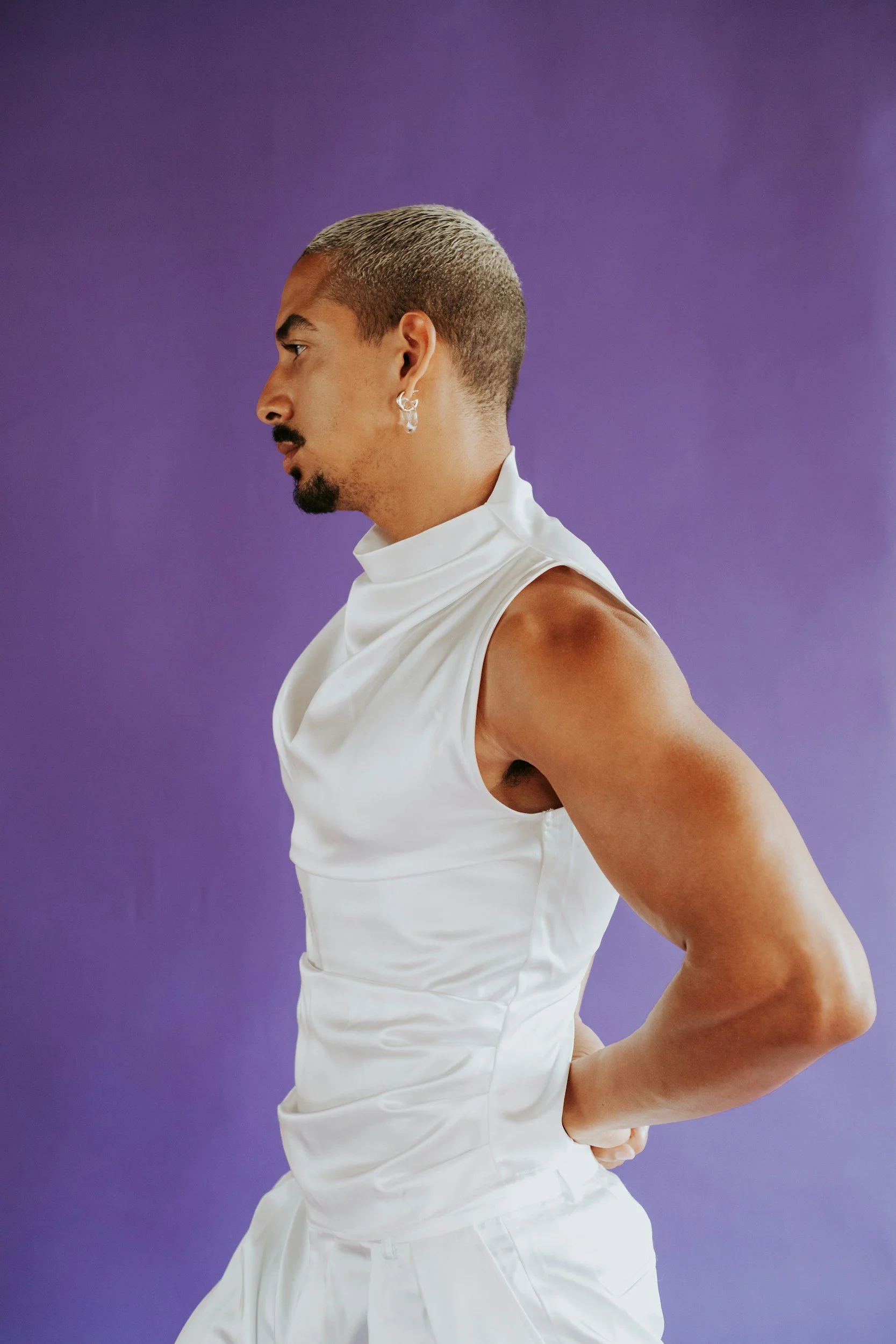 Gender-diverse person in white sleeveless top against purple background — affirming somatic therapy for nonbinary, gender-diverse, and queer adults in California