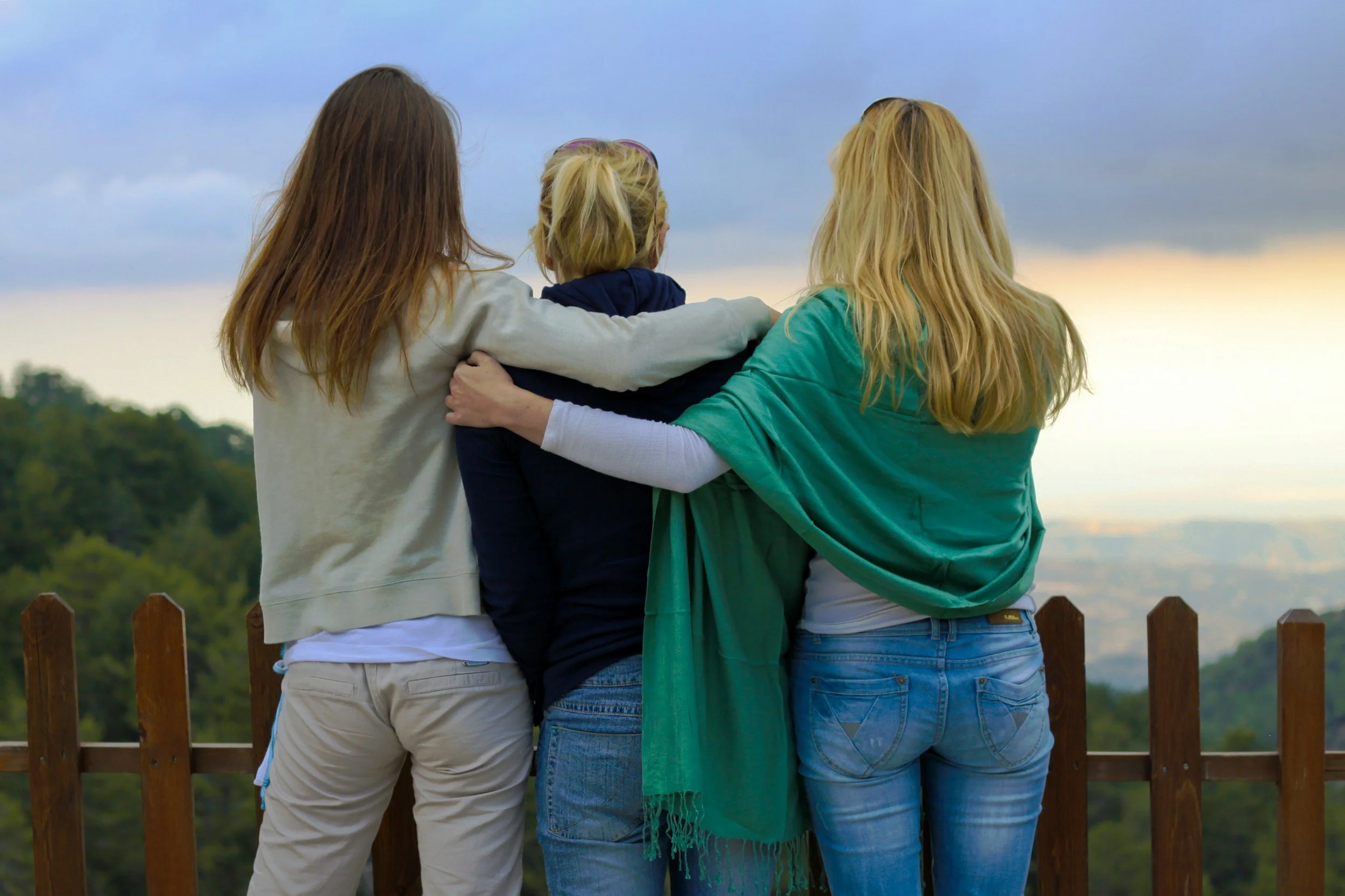Three people embracing from behind overlooking a scenic view — affirming therapy for polyamory, chosen family, and multiple-partner relationships in California