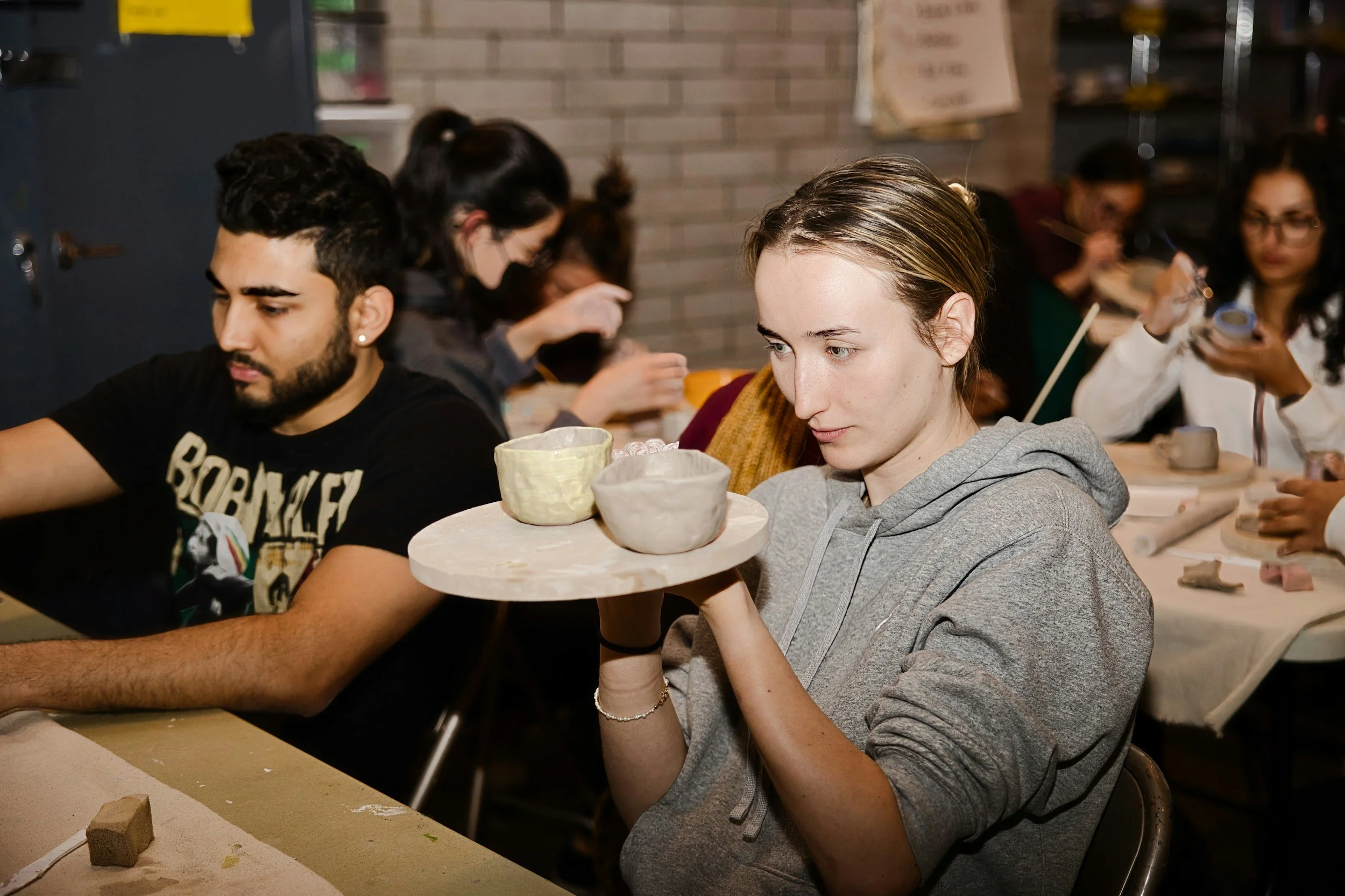 Art student carefully examining clay sculpture in graduate studio class — MFA and art school trauma, creative paralysis, and therapy for artists in California