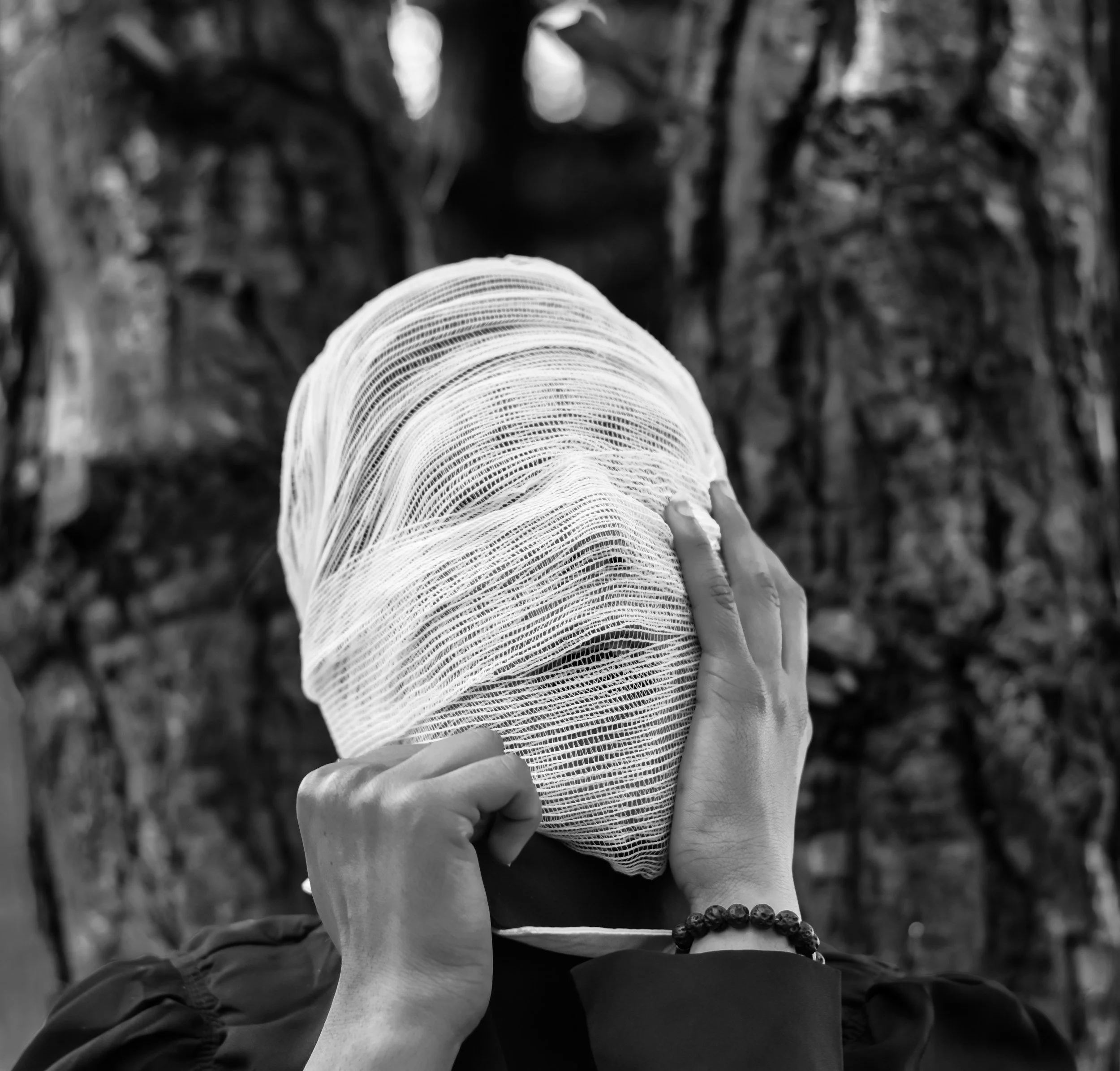 Black and white image of a figure with head wrapped in gauze bandage in a forest — creative paralysis, identity wounds, and healing from art school trauma through somatic therapy