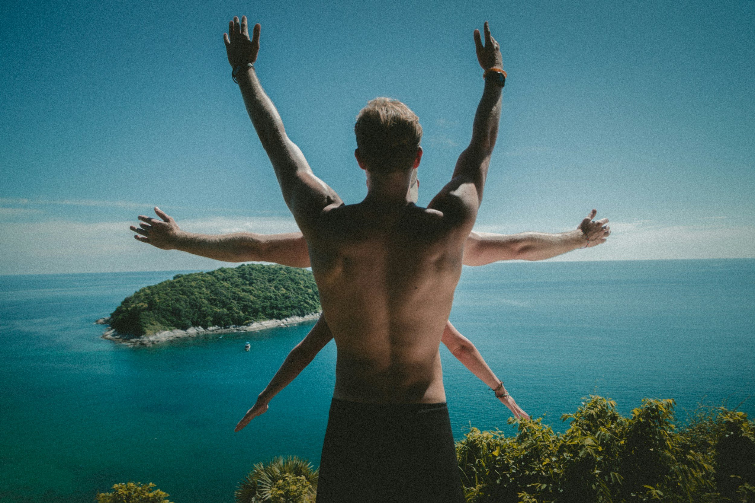 The back of a shirtless man with multiple arms outstretched in different directions against a blue ocean backdrop, resembling the Vitruvian Man.
