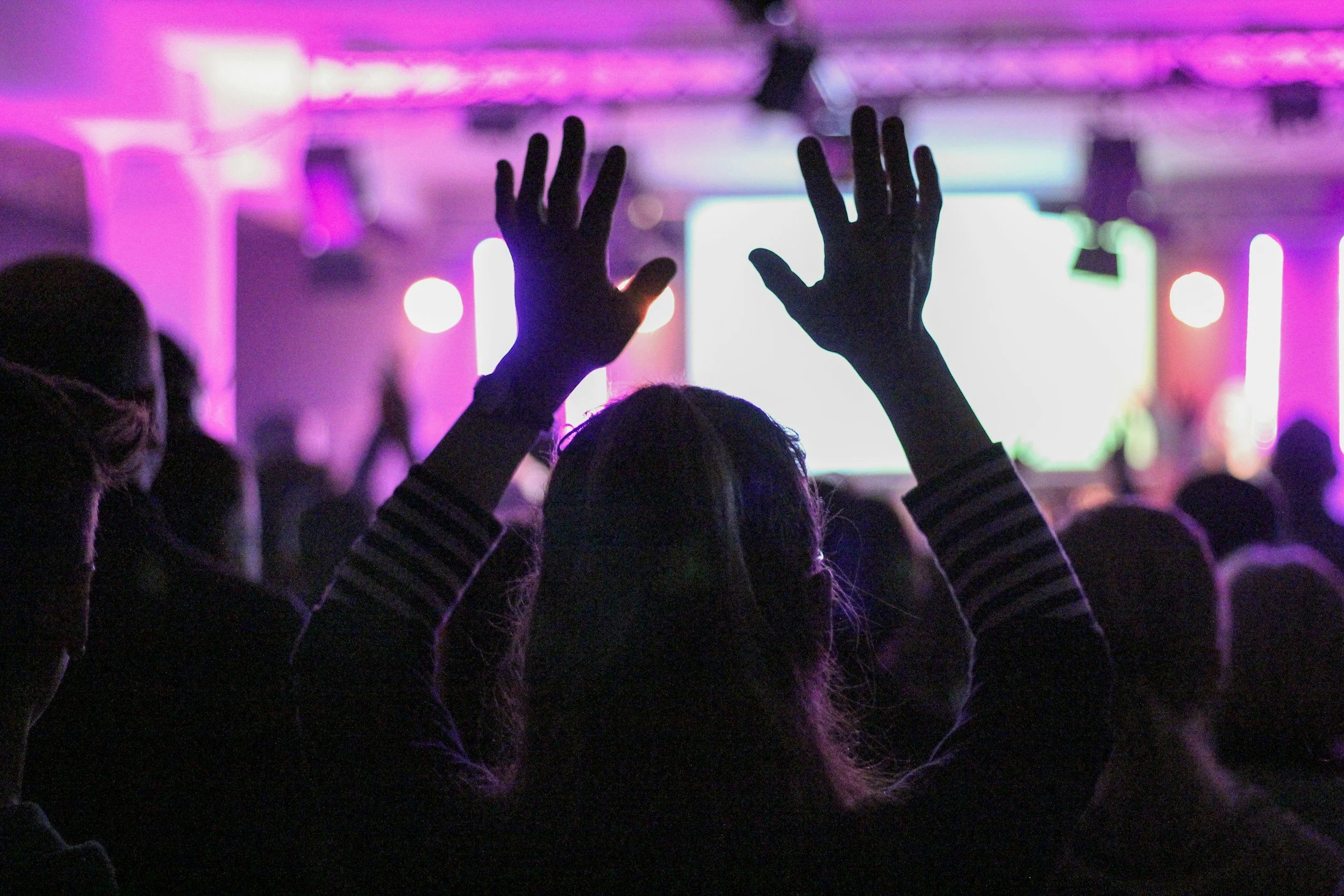Crowd with hands raised in worship under bright purple stage lighting, illustrating common signs of a high-control environment such as intense emotional pressure and group conformity.