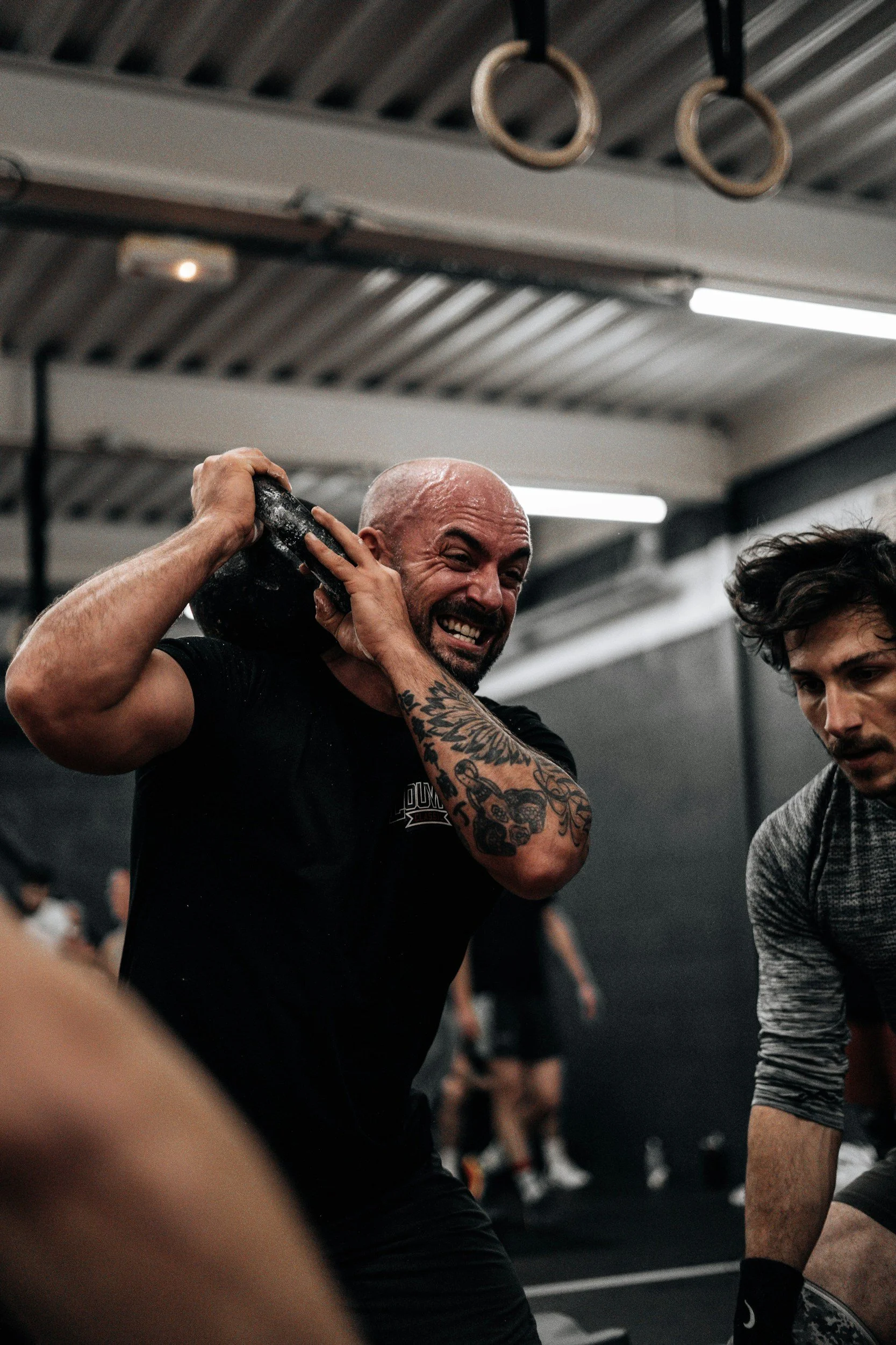 Man straining while lifting a heavy kettlebell in an intense gym setting, illustrating examples of high-control environments in fitness culture alongside churches, academia, cults, and relationships.