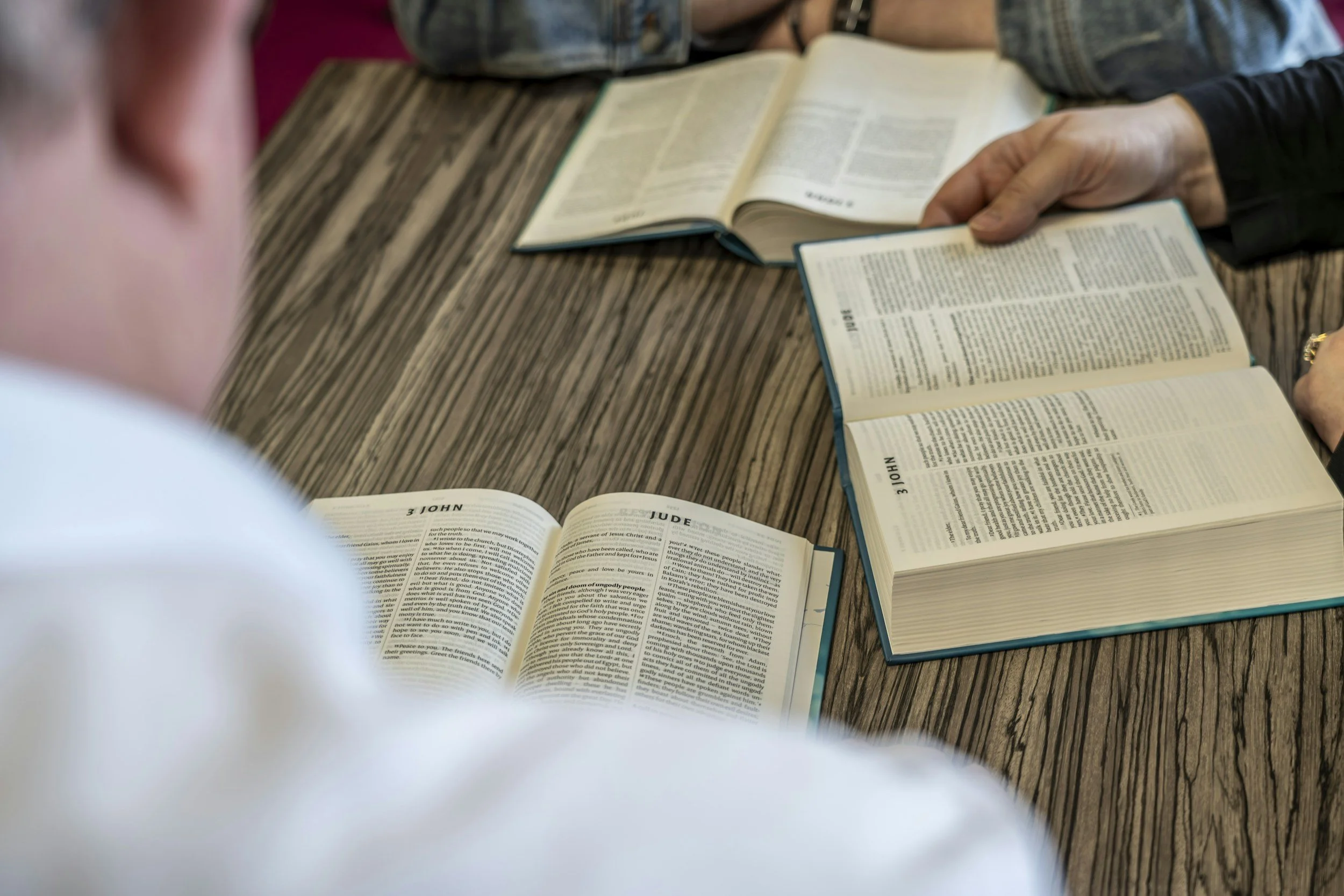 Group Bible study with several open Bibles on a wooden table, illustrating high-control churches and religious spaces built around close scripture study and group conformity.