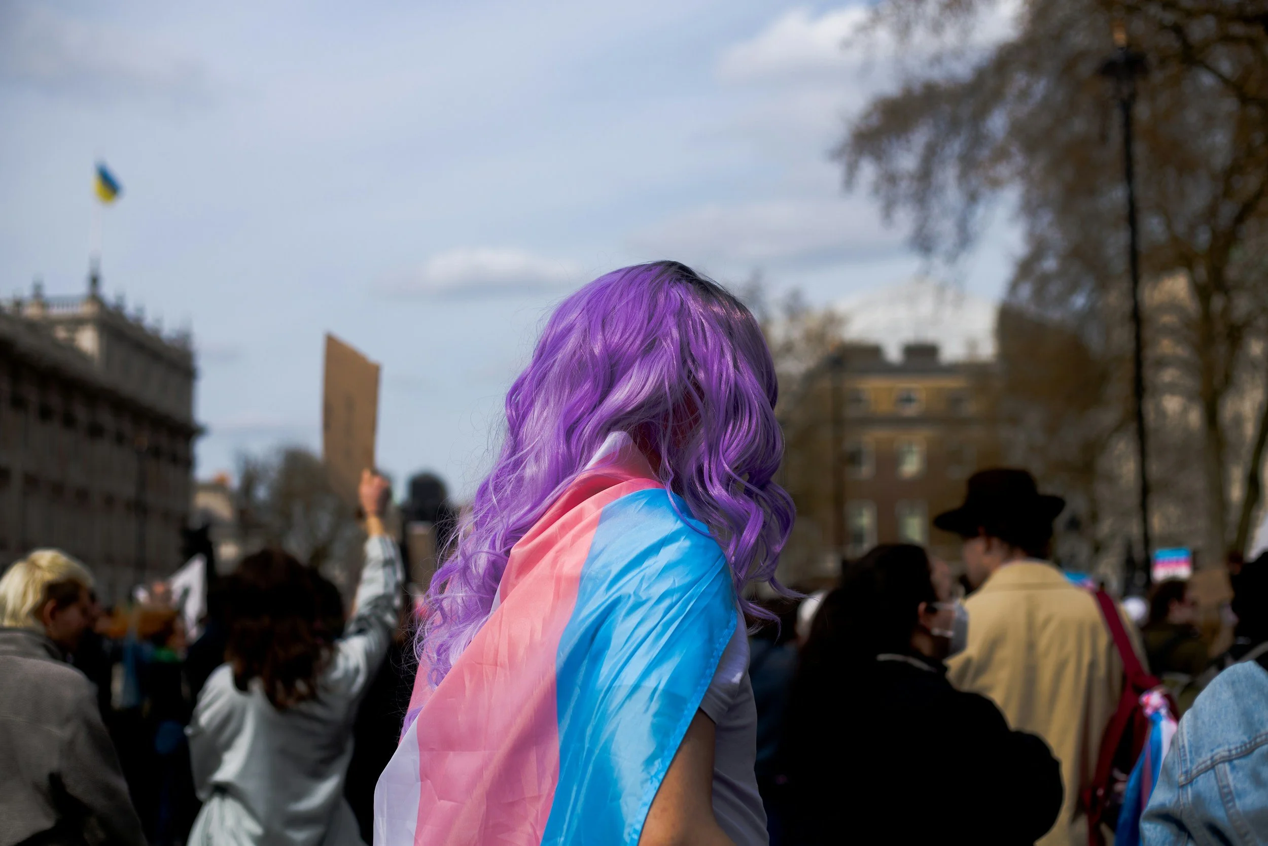 Person with purple hair draped in a transgender pride flag at a gathering, reflecting why queer and trans people may be vulnerable to high-control environments.
