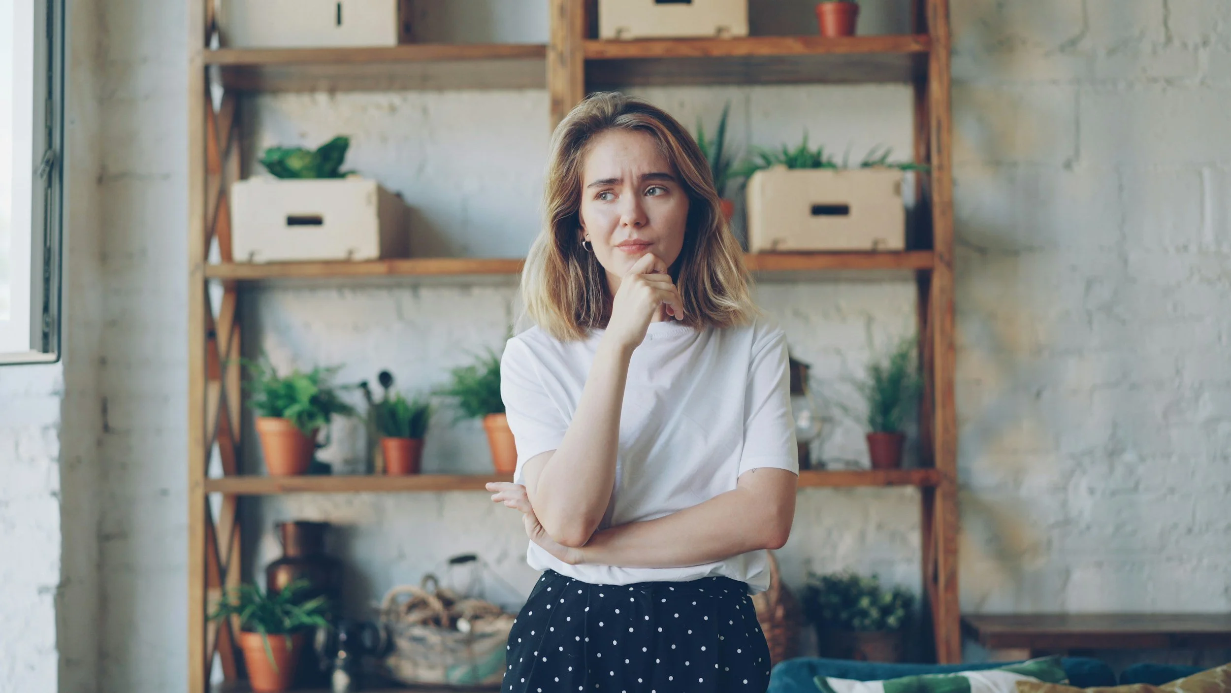 Woman standing indoors with a worried, thoughtful expression, weighing an uncertain decision