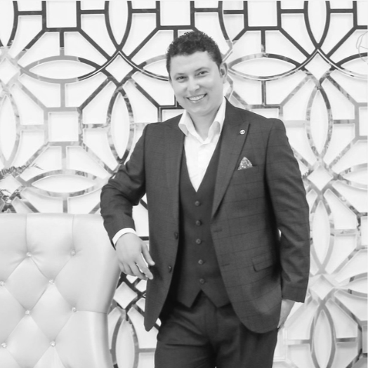 A young man in a suit standing in front of an intricate decorative wall, smiling at the camera.
