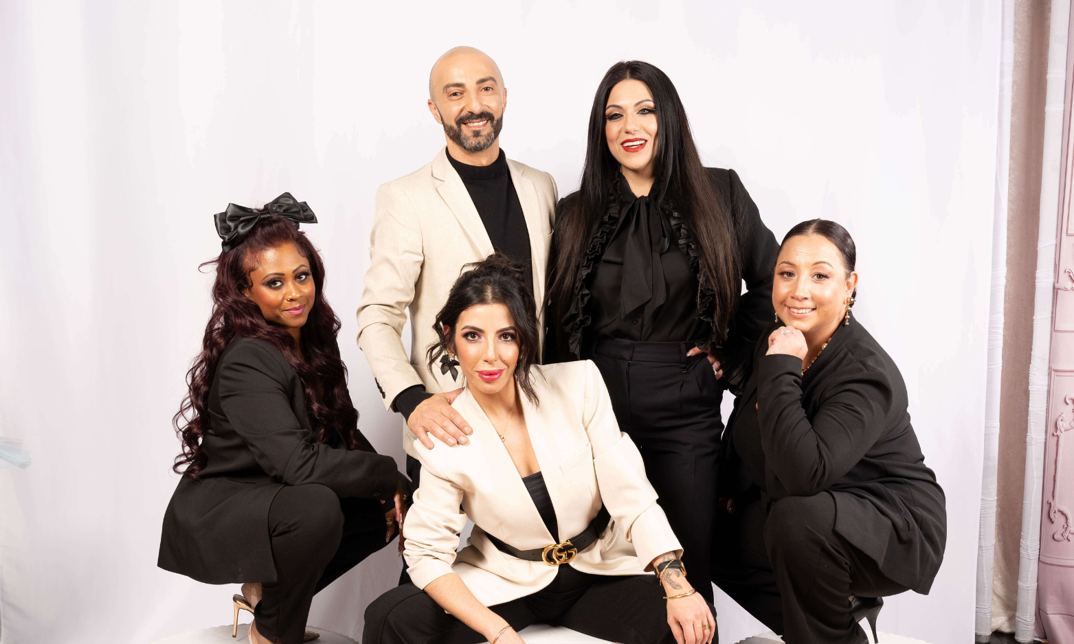 Five professionally dressed people posing for a group photo against a plain white backdrop, with three women and two men, smiling and looking at the camera.